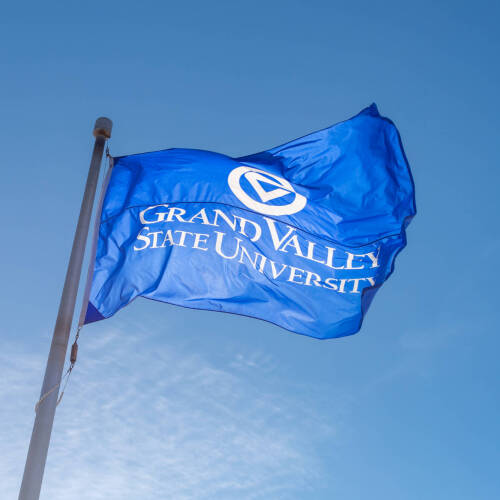 A flag with GVSU's logo flies in Allendale against a blue sky.